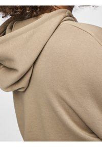 Felpa beige con una texture morbida, dotata di cappuccio con coulisse e una vestibilità comoda. Il tessuto presenta lievi pieghe e dettagli di cucitura.