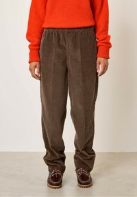 Rjave kordurojske hlače z sproščenim krojem, ki imajo elastičen pas in so v paru s temno rjavimi čevlji z rožnatimi vezalkami.