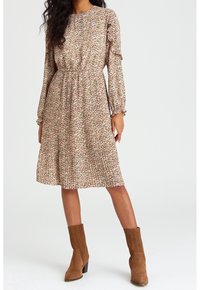 Robe à manches longues à motif floral en rose clair avec des accents verts, dotée d'une taille froncée et d'une jupe plissée. Bottines en suède marron.