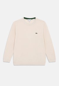 Pulover bej deschis cu guler rotund, mâneci lungi și tricot texturat. Are un mic logo cu crocodil verde pe partea stângă a pieptului.