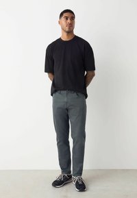 Camiseta negra de mangas cortas combinada con pantalones gris slim-fit y zapatillas negras, con una tela texturizada y un diseño minimalista.
