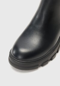 Botín de piel negra hasta el tobillo, con puntera redondeada, suela negra gruesa, textura sutil y acabado liso. Sin herrajes ni patrones visibles.