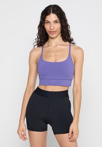 Fioletowy obcisły sportowy krótki top z cienkimi ramiączkami i logo przy krawędzi, w połączeniu z czarnymi szortami z wysokim stanem. Gładki, elastyczny materiał.