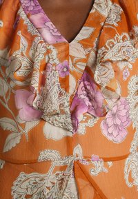 Oranžová kvetinová blúzka s V-výstrihom, volánikovým detailom a ľahkým, mierne priesvitným materiálom s ružovými a krémovými kvetinovými vzormi.