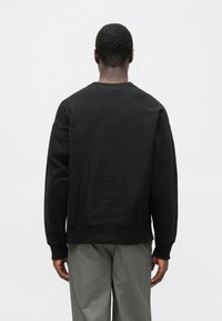 Μαύρο φούτερ με στρογγυλή λαιμόκοψη, μακριά μανίκια και ribbed μανσέτες. Ομαλή υφή, ελαφρώς φαρδιά εφαρμογή, μινιμαλιστικός σχεδιασμός.