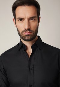 Czarna koszula zapinana na guziki z kołnierzem typu spread, teksturowana tkanina i sześć dopasowanych guzików z przodu. Prosty design, bez widocznych wzorów ani logo.