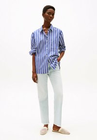 Camicia a righe blu e bianche, design con bottoni, maniche lunghe arrotolate, abbinata a jeans dritti blu chiaro e scarpe slip-on in tessuto beige.