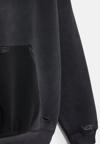 Fekete pulóver ujj- és zsebrész kis koptatott lyukakkal és látható varrással a szöveten és a mandzsettán.