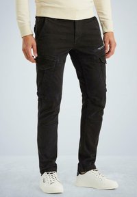Schwarze Cargo-Hosen mit mehreren Taschen, schlanker Schnitt und strukturiertem Stoff. Kombiniert mit weißen Sneakers mit schwarzen Akzenten.