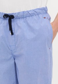 Modré a bílé kostkované kalhoty s elastickým pasem, nastavitelným černým šňůrkami, bočními kapsami a malým logem jako akcentem.