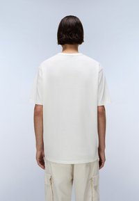 Tricou alb din bumbac cu croială lejeră, mâneci scurte și decolteu rotund. Asortat cu pantaloni cargo bej deschis. Design simplu, minimalist.