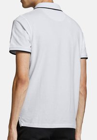 Witte polo met een klassieke kraag, korte mouwen en zwarte afwerking op de kraag en mouwranden. Honden textuur.