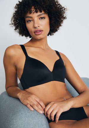 Black padded bra with a deep V-neck, adjustable straps, smooth fabric, and a minimalist design. Worn with matching black briefs.