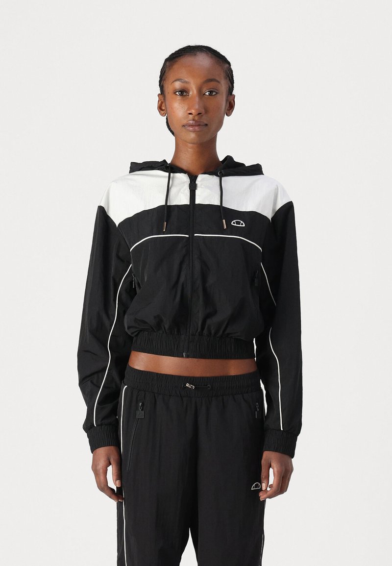 Cazadora corta en blanco y negro con capucha, que cuenta con cintura elástica, bolsillos laterales y franjas blancas en contraste en la tela.