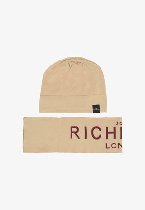 Beige gebreide muts en bijpassende sjaal, sjaal toont gedeeltelijk de donkerrode tekst "RICH", beide met kleine zwarte merketiketten.