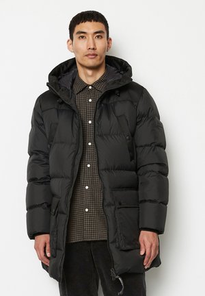 Schwarze Daunenjacke mit Kapuze, ausgestattet mit einem Reißverschluss vorne, seitlichen Taschen und einem gesteppten Design. Getragen über einem karierten Hemd.