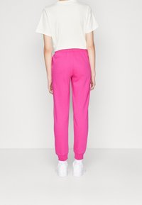 Pink cotton sweatpants with elastic waistband and cuffs, paired with white sneakers. The top is a loose-fit white t-shirt.