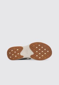 Parte inferior de un zapato con una base de goma clara, texturizada para mayor agarre. Presenta un diseño moldeado con patrones cuadrados y rectangulares, acentos en color marrón.
