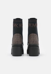 Bottines noires avec une tige en tricot extensible, ornées d'un motif monogramme marron à l'arrière et d'un talon épais pour plus de stabilité.