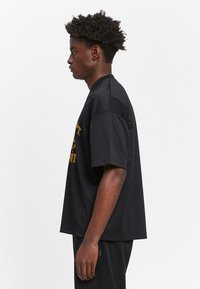 Black mesh oversized t-shirt with short sleeves, featuring yellow text on the front. Smooth texture and breathable design.