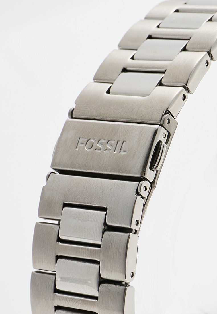 Bracelet en acier inoxydable avec des segments reliés, présentant une finition brossée et polie. Gravé "FOSSIL" sur un maillon.