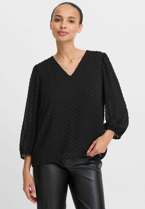 Schwarze Bluse aus strukturiertem Stoff mit V-Ausschnitt, weiten Ärmeln und gerafften Manschetten. Besitzt erhabene Punkte im gesamten Material.