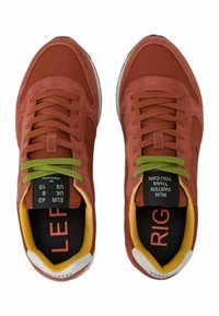 Sneakers rossi con una tomaia in tessuto testurizzato, lacci verdi, fodera gialla e suole interne nere a contrasto etichettate "SINISTRA" e "DESTRA."