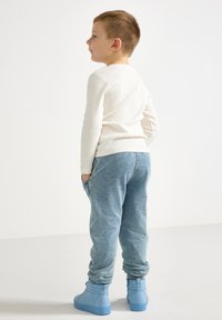 Hvit langermet skjorte kombinert med blå joggebukser og blå høye sneakers. Joggebuksene har et teksturert stoff og sidelommer.