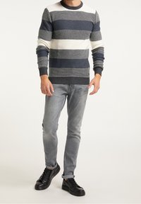 Maglione a righe in maglia nei colori blu navy, grigio e crema, con scollatura a girocollo, polsini e orlo a coste, abbinato a jeans grigi e sneaker nere.