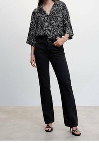 Sort skjorte med knapper og hvidt bladmønster, brede ærmer, parret med sorte flared jeans og sorte sandaler med stropper. Glat tekstur over det hele.