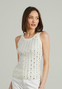 Top in cotone bianco a costine con righe verticali di paillettes metalliche che creano un motivo texture. Il collo è rotondo e senza maniche.