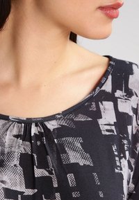 Svart och grå mönstrad topp med en avslappnad passform. Har en bred rund halsringning, texturerat tyg och diskreta veck vid bysten.