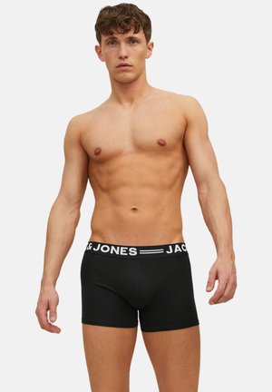 Boxer noirs avec une ceinture élastique blanche affichant le texte "JACK & JONES." Confectionnés en tissu lisse et extensible, coupe ajustée.
