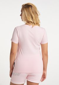 Helles rosa T-Shirt mit kurzen Ärmeln und klassischem Rundhalsausschnitt; der Stoff ist weich mit einer glatten Textur. Passende Shorts mit dezentem silbernem Schriftzug.