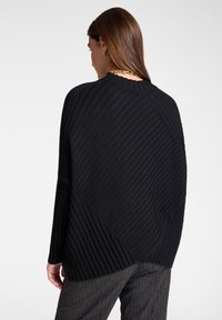 Suéter negro de canalé con textura diagonal y dobladillo redondeado, llevado sobre pantalones grises de rayas. Sin cierres o adornos visibles.