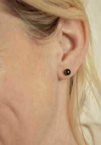 Närbild av en kvinnas öra med kort blont hår som bär en liten svart stiftörring.