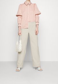 Blouse rose clair texturée avec manches bouffantes, fermeture à boutons sur le devant, et pantalon taille haute à carreaux blancs. Sac à main tressé blanc et sandales menthe.