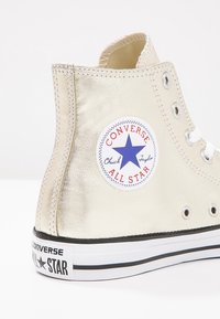 Sneakers alte in oro metallico con lacci bianchi e logo prominente Converse All Star. Presentano suola in gomma nera e occhielli in metallo.
