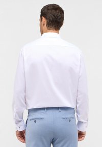 Weißes Langarmhemd mit einem normalen Kragen, ausgestattet mit geknöpften Manschetten. Kombiniert mit hellblauen Hosen aus einem strukturierten Stoff.