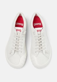 Άσπρα αθλητικά παπούτσια με δερμάτινη υφή, γκρι κορδόνια και κόκκινο εσωτερικό. Διαθέτουν στρογγυλεμένη μύτη και άσπρη ελαστική σόλα με διακοσμητικές λεπτομέρειες.