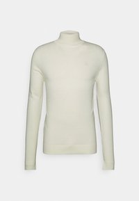 Halsringad tröja i krämfärg, tillverkad av mjukt stickat tyg. Har långa ärmar, en figurnära passform och en liten logodetalj på bröstet.