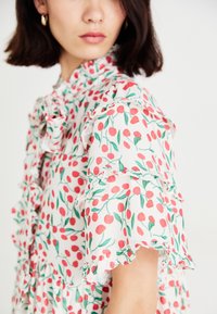 Vestido floral con fondo blanco, estampado de cerezas rojas, hojas verdes y mangas con volantes, hecho de un tejido ligero con un acabado texturizado.
