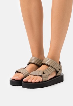 Sandales beiges avec des brides matelassées, bout ouvert et épaisse semelle noire. Équipées de brides ajustables pour un maintien sécurisé.