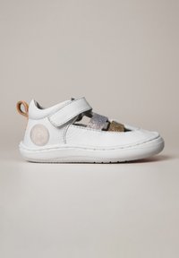 Chaussure en cuir blanche avec deux sangles ajustables, ornée d'accents argentés et dorés scintillants, semelle texturée et logo circulaire sur le côté.