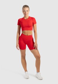 Rode twee-delige sportoutfit bestaande uit een aangesloten korte mouw crop top en hoge taille shorts. Zachte textuur en rekbare stof.