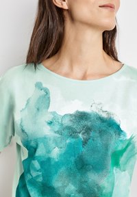 Top de manga corta en verde menta con un diseño acuarela en tonos de teal y verde oscuro, con un corte relajado y escote redondo.