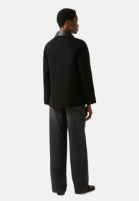 Sort uldblandet jakke med læderkrave, afslappet pasform og grå straight-fit jeans med sidelommer og glat tekstur.