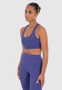 Paarse sportbeha en high-waisted leggings, beide gemaakt van gladde, rekbare stof. Bevat minimale merknaam op de tailleband.