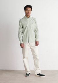 Light green button-up shirt, white trousers, and dark green sneakers. Shirt features a collar and buttons, with a logo on the chest.