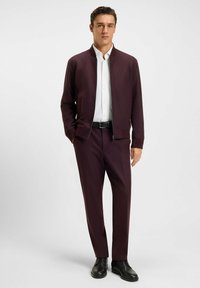 Bordeaux zip-up bomberjack over een wit shirt, gecombineerd met bijpassende bordeaux pantalon en zwarte dresschoenen. Glad materiaal, slim fit.